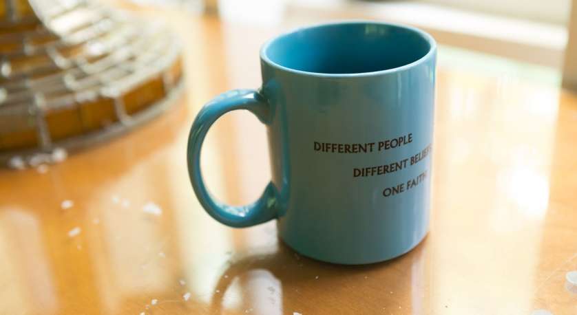 coffee mug on a table that says "different people, different beliefs, one faith"